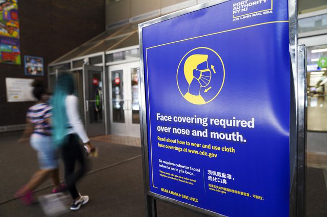 People walk past a notice of face covering requirement at the entrance to Port Authority Bus Terminal in New York on August 9th, 2020.